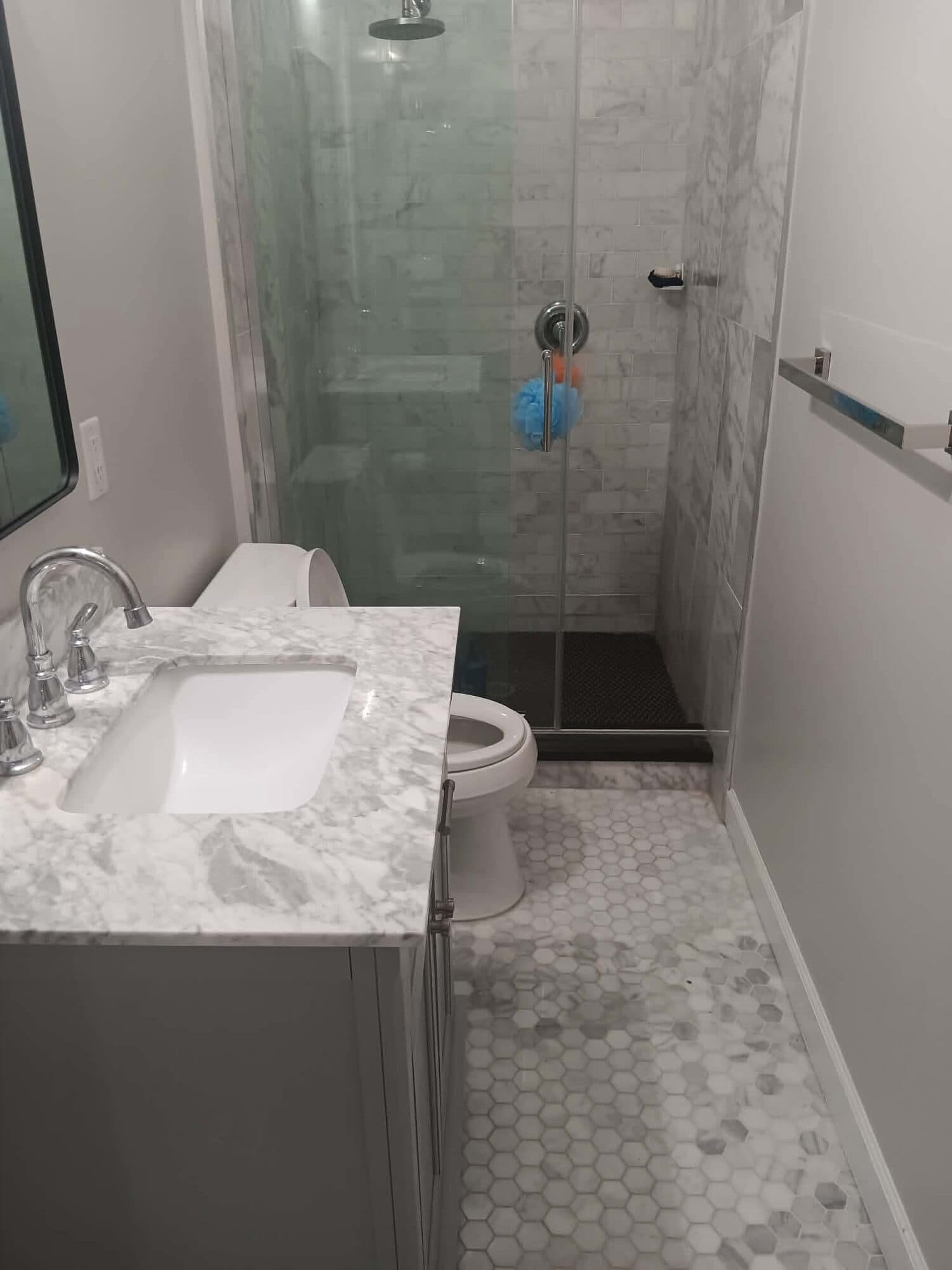 Clean bathroom with a marble vanity, glass shower and hex tile floor