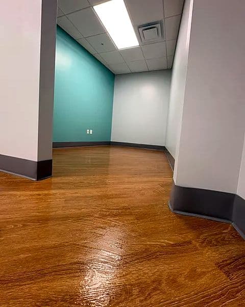 High-gloss wood-look floor reflecting the light down a clean office corridor with a teal wall