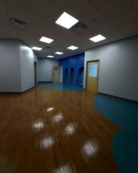 Wide hallway with a curved floor inlay and ceiling lights reflected in the polished floor
