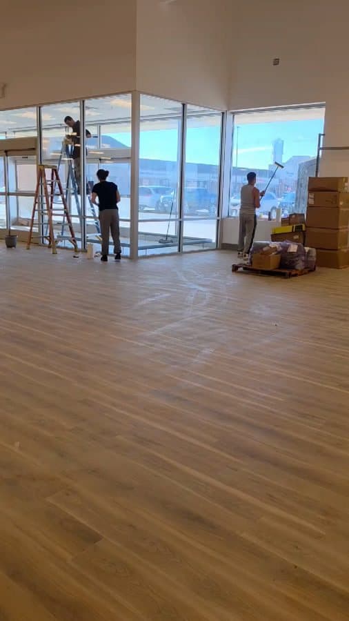 Three crew members on ladders cleaning tall storefront windows in a retail build-out