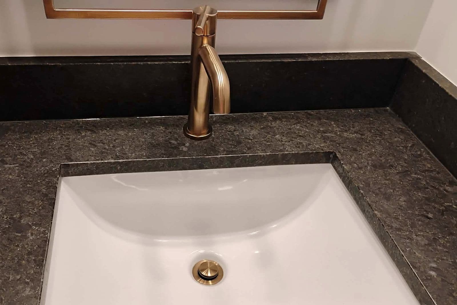 Spotless white undermount sink with a brushed gold faucet on dark granite
